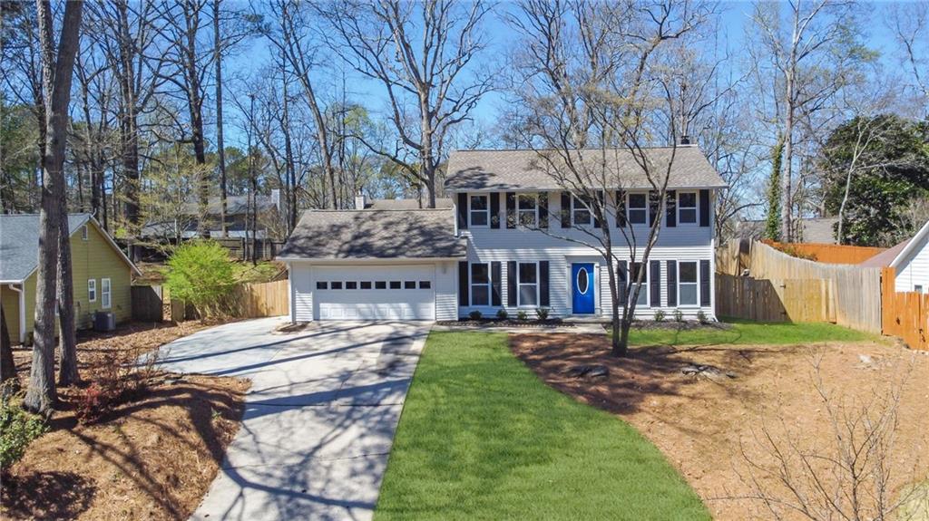 colonial home featuring fence, concrete driveway, a front yard, a shingled roof, and an attached garage