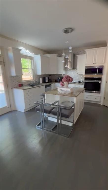 kitchen featuring stainless steel appliances, white cabinets, decorative backsplash, and wall chimney range hood