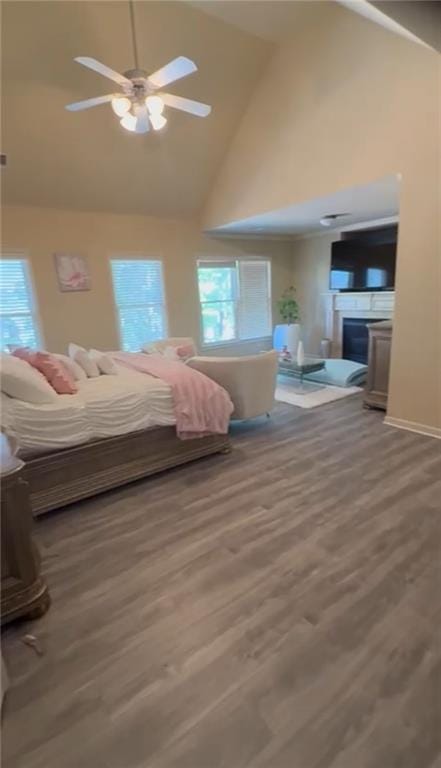 bedroom featuring high vaulted ceiling, a fireplace, wood finished floors, and a ceiling fan