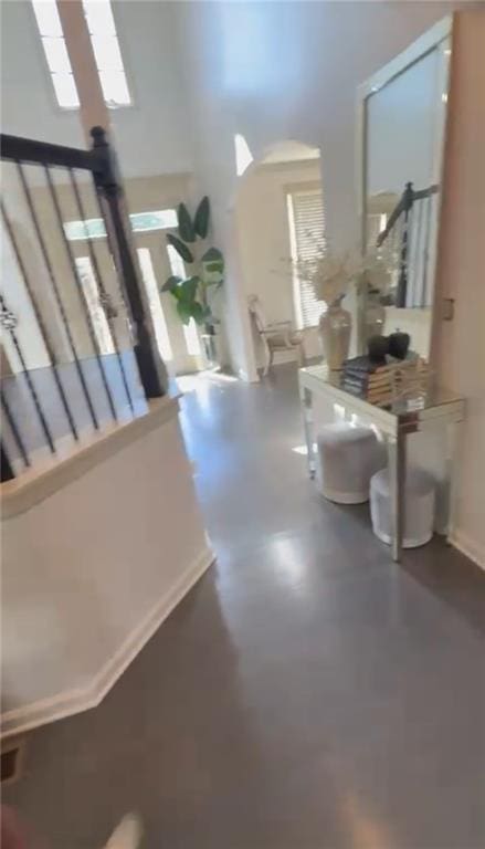 hallway with a high ceiling, healthy amount of natural light, stairs, and concrete flooring
