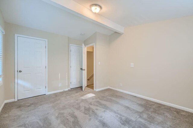 unfurnished bedroom with beam ceiling and light carpet