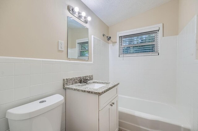 full bathroom with toilet, tiled shower / bath, vanity, a textured ceiling, and tile walls