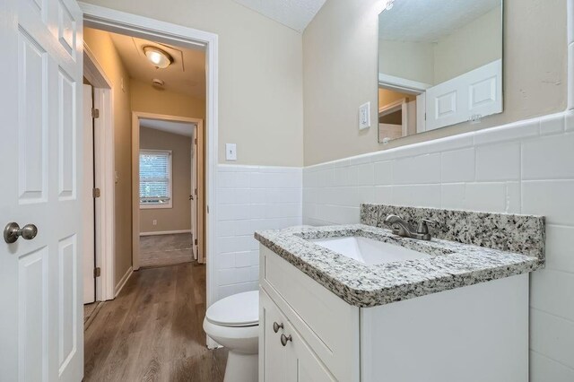 bathroom featuring vanity, hardwood / wood-style floors, tile walls, toilet, and decorative backsplash