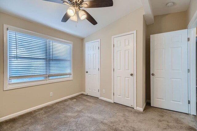 unfurnished bedroom with light carpet, vaulted ceiling, multiple closets, and ceiling fan