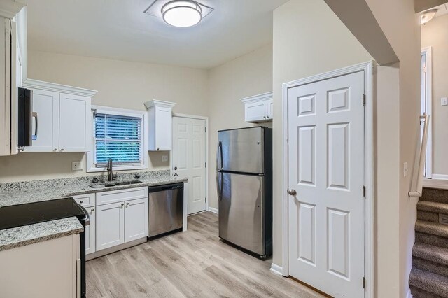 kitchen with light hardwood / wood-style floors, stainless steel appliances, sink, light stone counters, and white cabinets