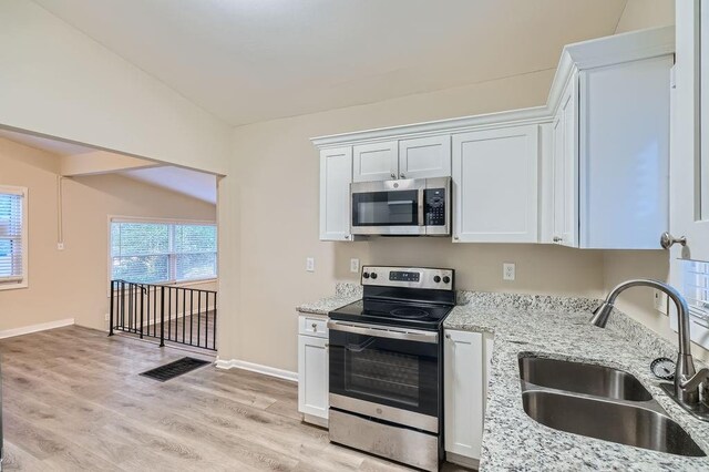 kitchen featuring light hardwood / wood-style flooring, vaulted ceiling, sink, appliances with stainless steel finishes, and white cabinets