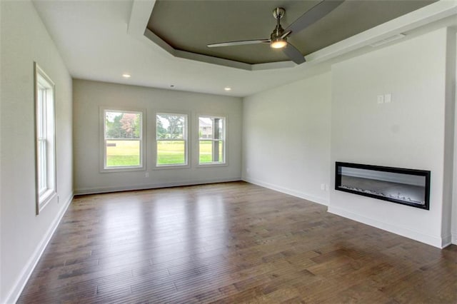 3065 Reserve Ct SW, Conyers, GA 30094 - unfurnished living room featuring a glass covered fireplace, ceiling fan, a raised ceiling, wood finished floors, and baseboards