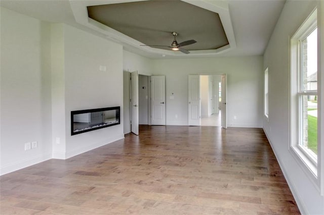 3065 Reserve Ct SW, Conyers, GA 30094 - unfurnished living room with a tray ceiling, a glass covered fireplace, ceiling fan, wood finished floors, and baseboards