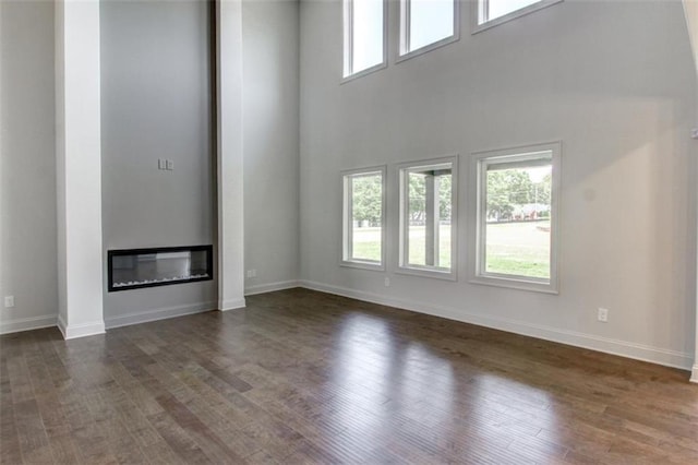 3065 Reserve Ct SW, Conyers, GA 30094 - unfurnished living room with dark wood-style floors, a towering ceiling, baseboards, and a glass covered fireplace