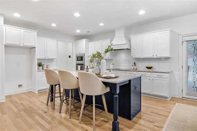 kitchen with a kitchen breakfast bar, a center island with sink, appliances with stainless steel finishes, premium range hood, and white cabinetry