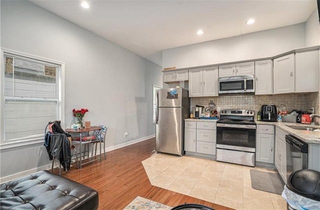 kitchen with light stone countertops, decorative backsplash, stainless steel appliances, and a sink