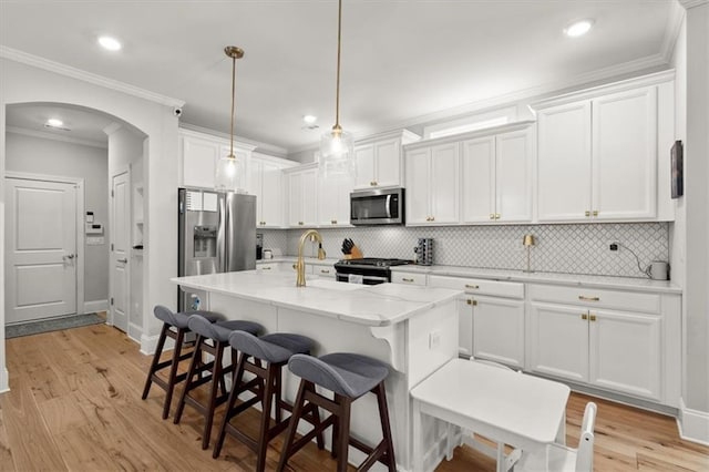 kitchen with light stone counters, pendant lighting, appliances with stainless steel finishes, a kitchen island with sink, and white cabinets