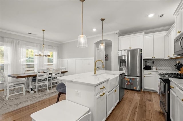 kitchen featuring appliances with stainless steel finishes, white cabinets, a center island with sink, and hanging light fixtures