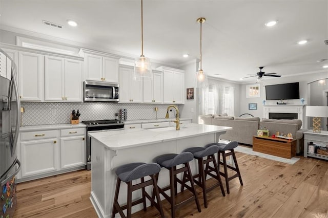 kitchen with pendant lighting, stainless steel appliances, open floor plan, white cabinets, and a sink