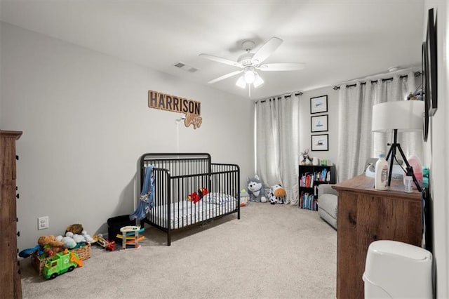 bedroom featuring visible vents, ceiling fan, a crib, and carpet flooring