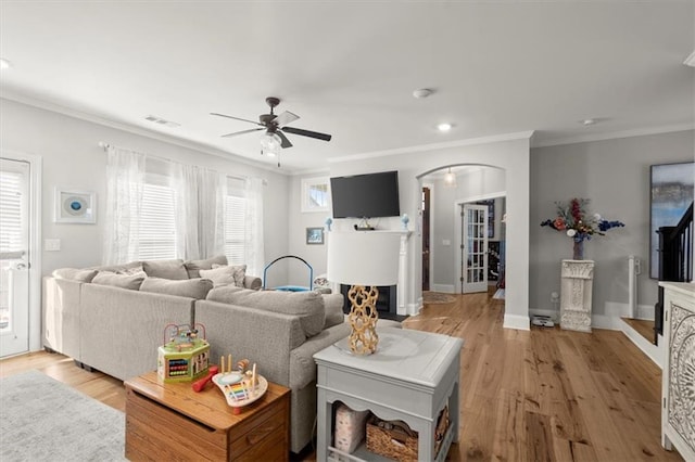 living room featuring baseboards, light wood-style flooring, arched walkways, and crown molding