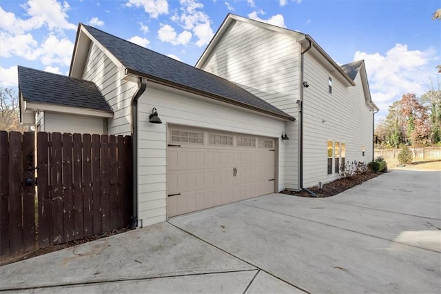 view of side of home with a garage, driveway, fence, and a shingled roof