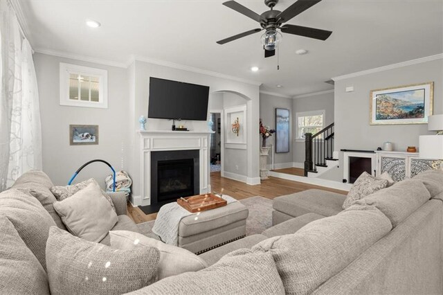 living area with a fireplace with flush hearth, baseboards, light wood-style floors, stairway, and crown molding