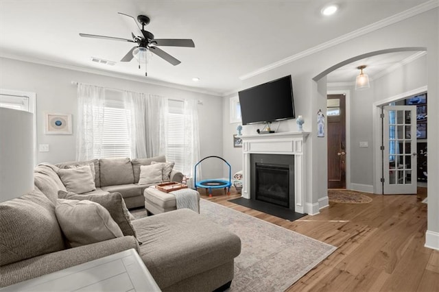 living area featuring arched walkways, a fireplace with flush hearth, ornamental molding, light wood-type flooring, and baseboards