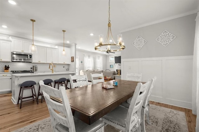 dining room with a wainscoted wall, light wood finished floors, recessed lighting, a decorative wall, and ornamental molding