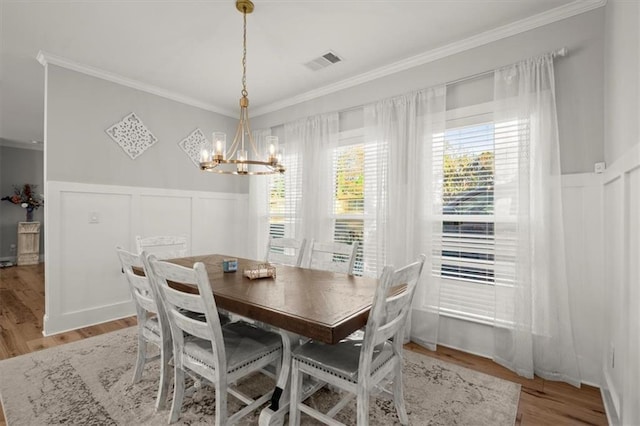 dining room featuring a wainscoted wall, visible vents, crown molding, and wood finished floors