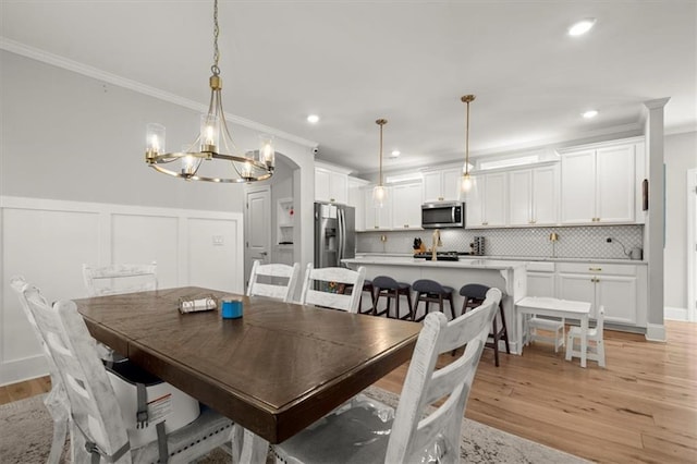 dining area with light wood-type flooring, a wainscoted wall, crown molding, and a decorative wall