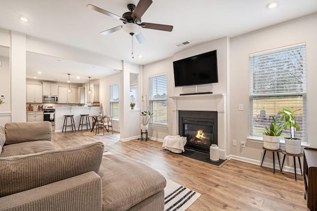 living room with plenty of natural light, light hardwood / wood-style floors, and ceiling fan