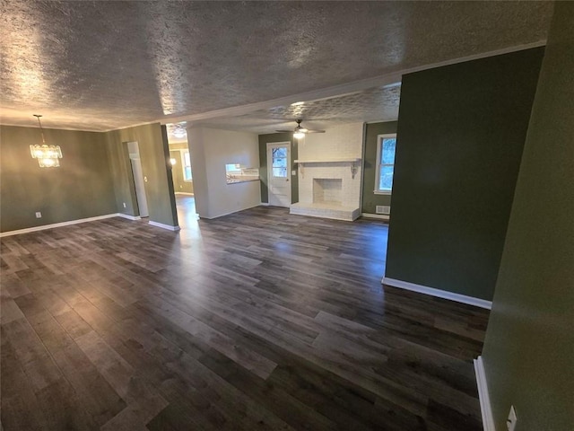 unfurnished living room featuring a brick fireplace, ceiling fan with notable chandelier, dark wood-type flooring, and a textured ceiling