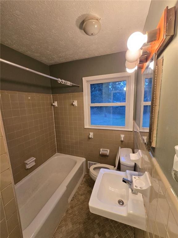 full bathroom with sink, tile walls, tiled shower / bath combo, toilet, and a textured ceiling