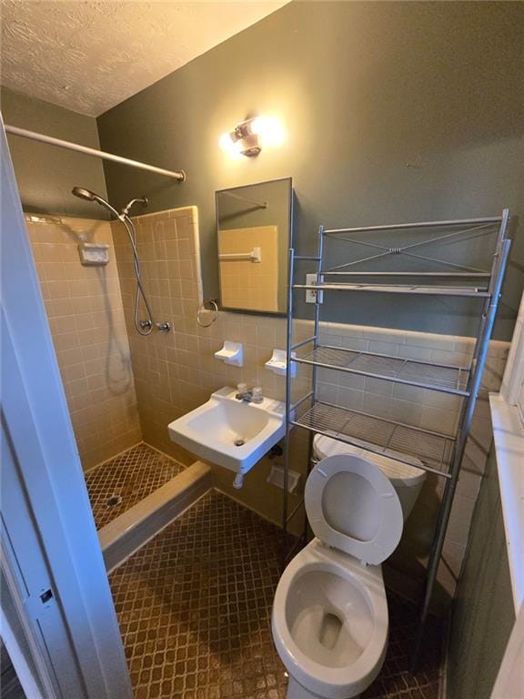 bathroom with sink, tile walls, tiled shower, toilet, and tile patterned floors