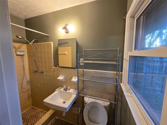 bathroom with sink, tile walls, a tile shower, a textured ceiling, and toilet