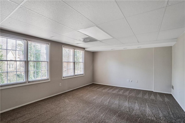 empty room featuring dark colored carpet, a drop ceiling, and baseboards