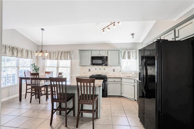 kitchen featuring lofted ceiling, light tile patterned flooring, hanging light fixtures, black appliances, and tasteful backsplash