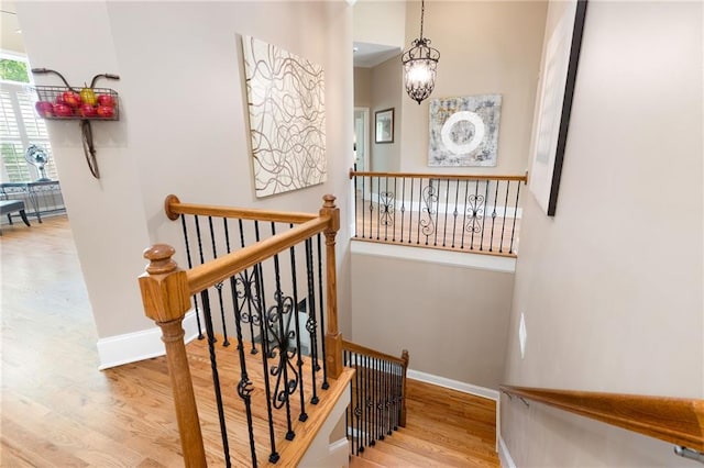 staircase featuring baseboards, wood finished floors, and a chandelier