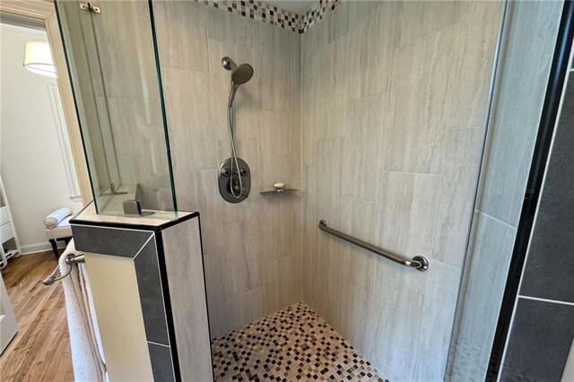bathroom with a tile shower, baseboards, and wood finished floors