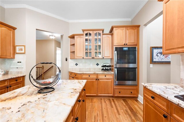 kitchen with light wood-type flooring, stainless steel double oven, glass insert cabinets, and tasteful backsplash