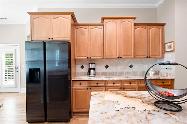 kitchen featuring light stone counters, light wood-type flooring, crown molding, tasteful backsplash, and black fridge