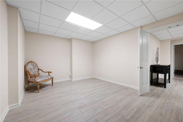 living area with baseboards, a paneled ceiling, and light wood-type flooring