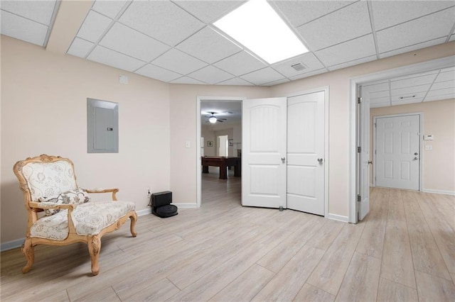 living area with visible vents, light wood-style floors, electric panel, baseboards, and a paneled ceiling