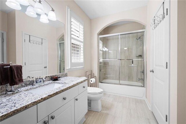 bathroom with combined bath / shower with glass door, vanity, and toilet