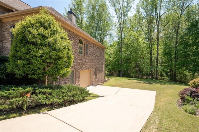 view of home's exterior with a chimney, concrete driveway, a garage, brick siding, and a yard
