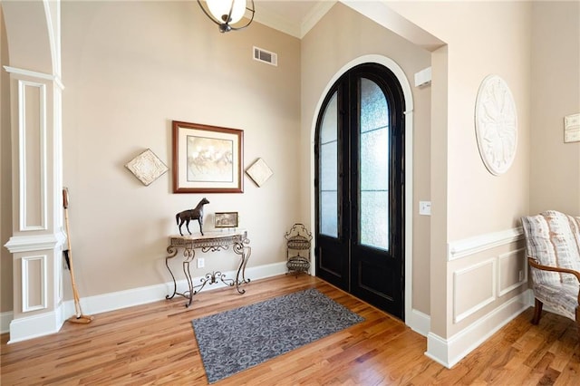 foyer entrance featuring visible vents, arched walkways, light wood-type flooring, crown molding, and decorative columns