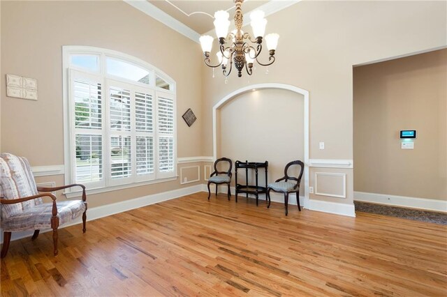 sitting room featuring arched walkways, an inviting chandelier, crown molding, and light wood-style flooring