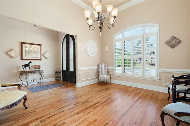 sitting room featuring a decorative wall, wood finished floors, wainscoting, a chandelier, and ornamental molding
