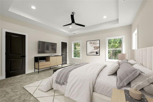 bedroom featuring ceiling fan, a raised ceiling, and light carpet