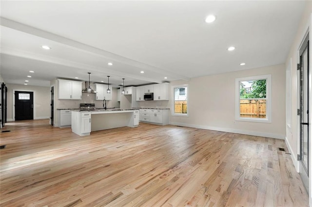 kitchen featuring appliances with stainless steel finishes, white cabinets, a kitchen island, pendant lighting, and light hardwood / wood-style flooring