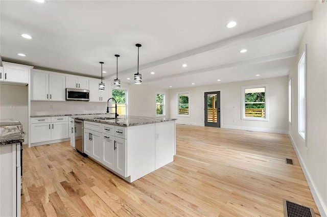 kitchen with sink, an island with sink, hanging light fixtures, appliances with stainless steel finishes, and dark stone countertops