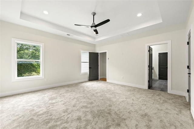 unfurnished bedroom with a raised ceiling, light carpet, ceiling fan, and ensuite bathroom