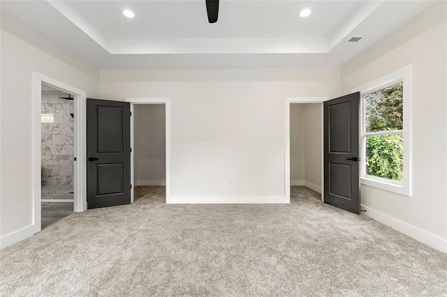 unfurnished bedroom with light carpet, a tray ceiling, connected bathroom, and ceiling fan