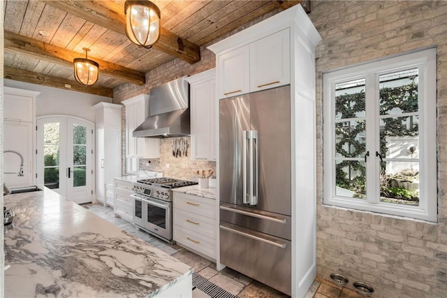 kitchen with french doors, wall chimney exhaust hood, premium appliances, beam ceiling, and decorative light fixtures